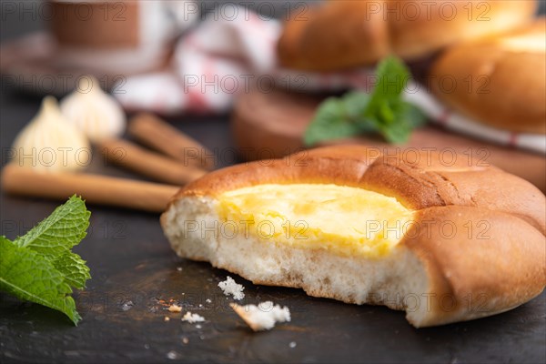 Sour cream bun with cup of coffee on a black concrete background and linen textile. Side view, close up, selective focus