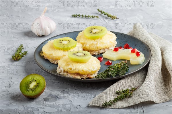 Pieces of baked pork with pineapple, cheese and kiwi on gray background, side view, close up