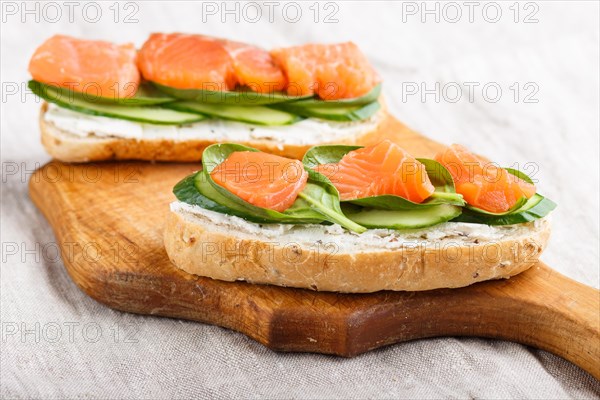 Smoked salmon sandwiches with cucumber and spinach on wooden board on a linen background. side view, close up