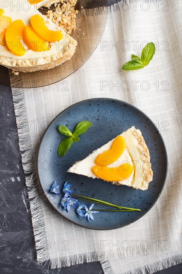 A piece of peach cheesecake on a blue ceramic plate with blue flowers on a linen napkin on a black concrete background. top view, copy space