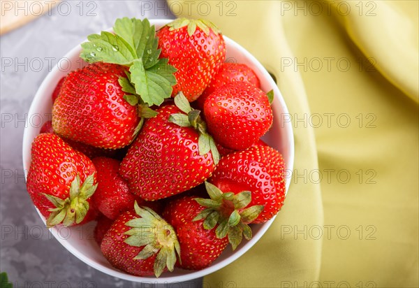 Fresh red strawberry in white bowl on gray concrete background. top view, close up, flat lay