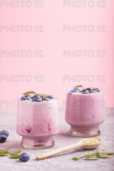 Yoghurt with blueberry and sesame in a glass and wooden spoon on gray and pink background. side view, close up