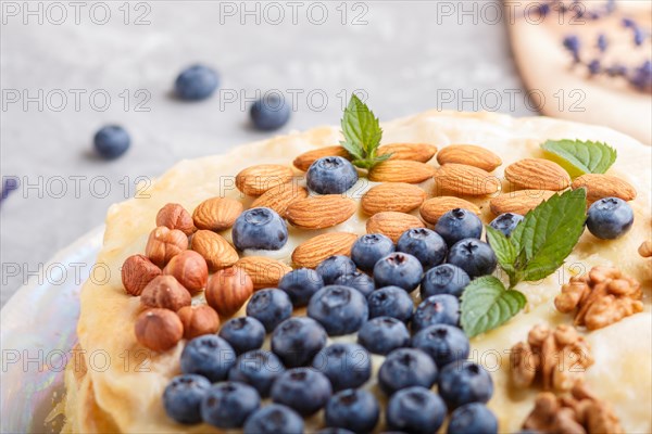 Homemade layered Napoleon cake with milk cream. Decorated with blueberry, almonds, walnuts, hazelnuts, mint on a gray concrete background. side view, selective focus, close up