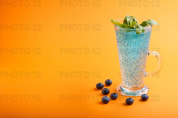 Glass of blueberry blue colored drink with basil seeds on orange background. Morninig, spring, healthy drink concept. Side view, selective focus, copy space