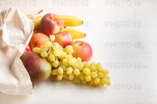 Fruits in reusable cotton textile white bag. Zero waste shopping, storage and recycling concept, eco friendly lifestyle. Side view, copy space. Peach, apple, mango, grape, banana