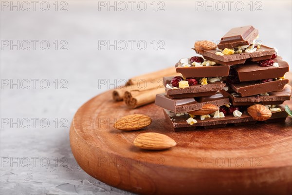 A pieces of milk chocolate with almonds and dried fruits on a brown wooden board on a gray concrete background. side view, close up, selective focus, copy space