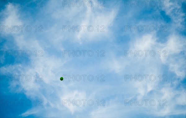 Green balloon from a St. Patrick's Day festival floating away in a blue sky filled with wispy white clouds in South Korea