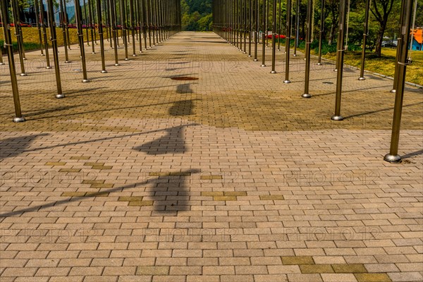 Shadows of flags on brick walkway between rows of chrome flagpoles in South Korea