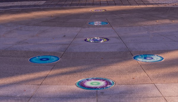 Arrow of round glass tiles of blue, purple, yellow and white inlaid in concrete sidewalk in public park in South Korea