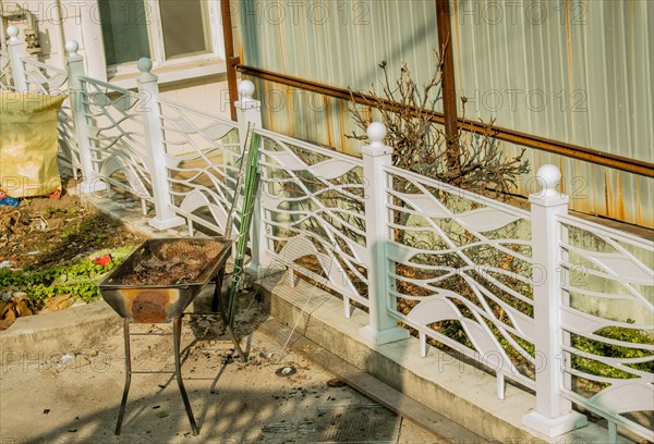 Dirty old outdoor barbeque grill on concrete patio next to white fence in South Korea