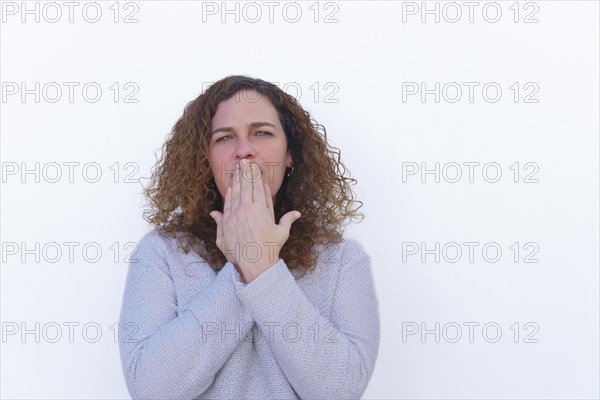Attractive blonde woman with curly hair and blue eyes covering her mouth with her hands looking at the camera with white background and copy space