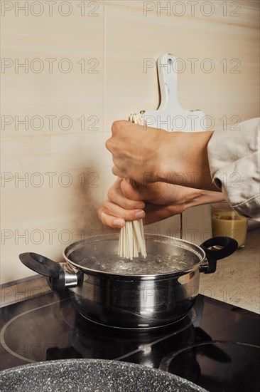 Unrecognizable woman putting rice noodles into boiling water