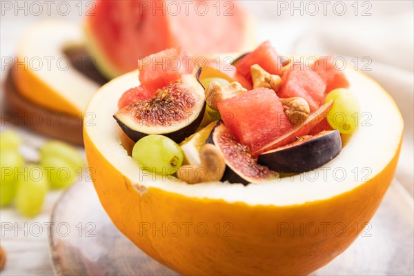 Vegetarian fruit salad of watermelon, grapes, figs, pear, orange, cashew on white wooden background and linen textile. Side view, close up, selective focus