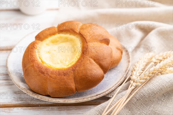 Sour cream bun with cup of coffee on a white wooden background and linen textile. Side view, close up, selective focus