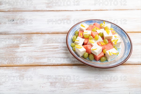 Vegetarian salad with watermelon, feta cheese, and grapes on blue ceramic plate on white wooden background. Side view, copy space