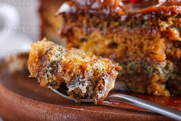 A piece of cake with caramel cream cutted with spoon on a wooden kitchen board and a cup of coffee, brown wooden background, close up, selective focus