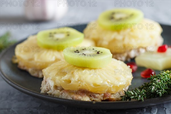 Pieces of baked pork with pineapple, cheese and kiwi on gray background, side view, close up, selective focus