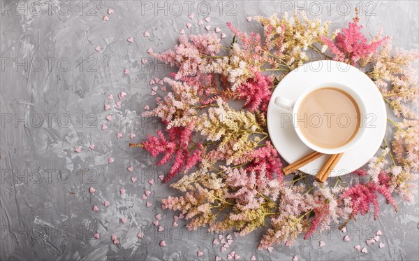 Pink and red astilbe flowers and a cup of coffee on a gray concrete background. Morninig, spring, fashion composition. Flat lay, top view, copy space
