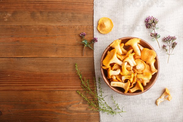 Chanterelle mushrooms in wooden bowl and spice herbs on wooden background with linen textile. top view, copy space, flat lay