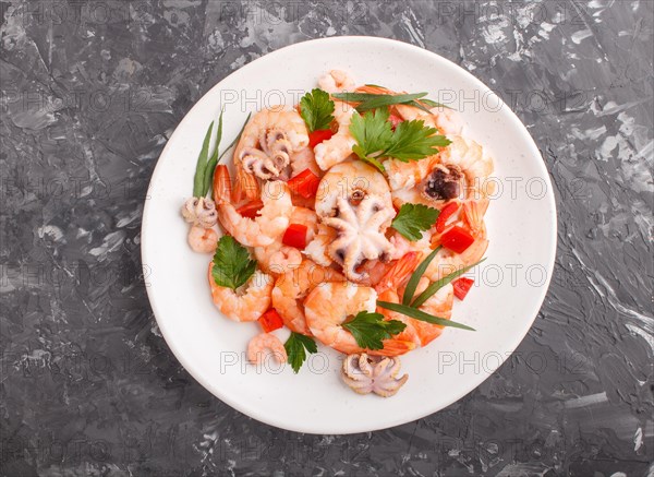 Boiled shrimps or prawns and small octopuses with herbs on white ceramic plate on a black concrete background. Top view, flat lay, close up