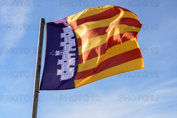 A vibrant flag with red and yellow stripes along a blue background with an emblem, against a blue sky, Majorca, Balearic Islands, Spain, Europe