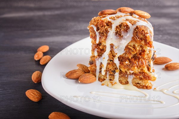 Pie with caramel, white milk sauce and almonds on a white plate on a black wooden background. close up