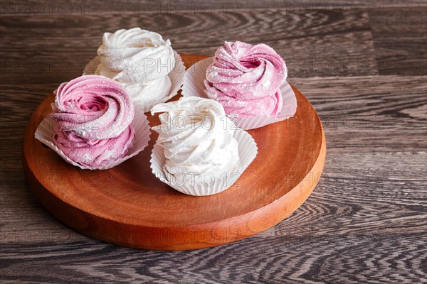 Pink and white marshmallows on a round wooden board on a gray wooden background. selective focus