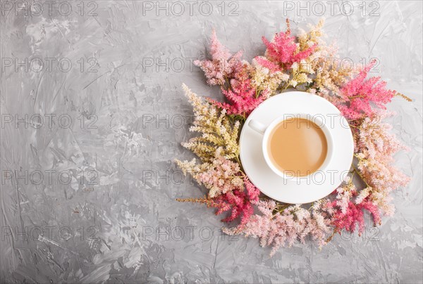 Pink and red astilbe flowers and a cup of coffee on a gray concrete background. Morninig, spring, fashion composition. Flat lay, top view, copy space