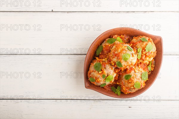 Pork meatballs with tomato sauce, oregano leaves, spices and herbs in clay bowl on a white wooden background. top view, flat lay, copy space