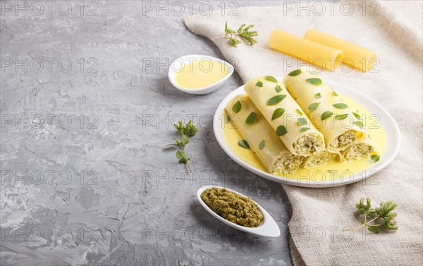 Cannelloni pasta with egg sauce, cream cheese and oregano leaves on a gray concrete background with linen textile. side view, close up, copy space