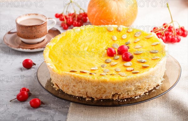 Traditional american sweet pumpkin pie decorated with hawthorn red berries and pumpkin seeds with cup of coffee on a gray concrete background. side view, close up, selective focus