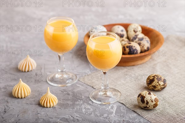 Sweet egg liqueur in glass with quail eggs and meringues on a gray concrete background. Side view, close up