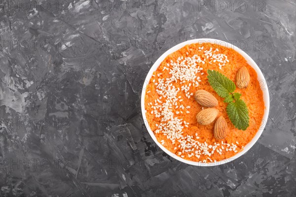 Carrot cream soup with sesame seeds and almonds in white bowl on a black concrete background. top view, flat lay, copy space