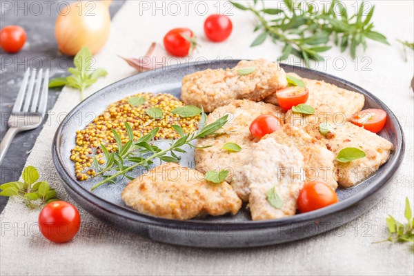 Fried pork chops with tomatoes and herbs on a gray ceramic plate on a black concrete background and linen textile. side view, close up, selective focus