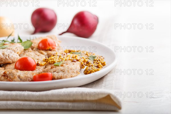 Fried pork chops with tomatoes and herbs on a white ceramic plate on a white wooden background and linen textile. side view, close up, selective focus