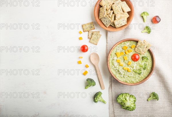 Green broccoli cream soup with crackers and cheese in wooden bowl on a white wooden background and linen napkin. top view, flat lay, copy space