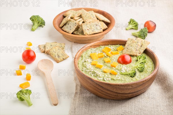 Green broccoli cream soup with crackers and cheese in wooden bowl on a white wooden background and linen napkin. side view, close up