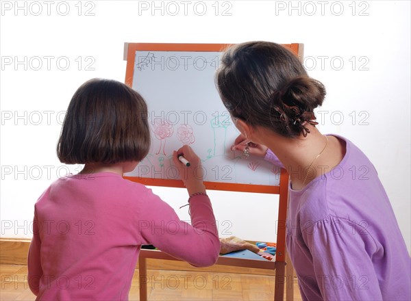 Two children are focused on drawing on a paper affixed to an easel with colorful markers, Youngs girls drawing on the white board