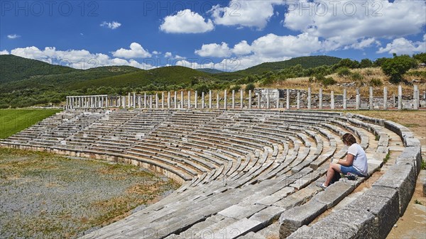 Person sitting in ancient stadium under clear blue sky with mountains in the background, Archaeological site, Ancient Messene, capital of Messinia, Messini, Peloponnese, Greece, Europe