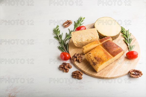 Smoked cheese and various types of cheese with rosemary and tomatoes on wooden board on a white wooden background. Side view, close up, copy space
