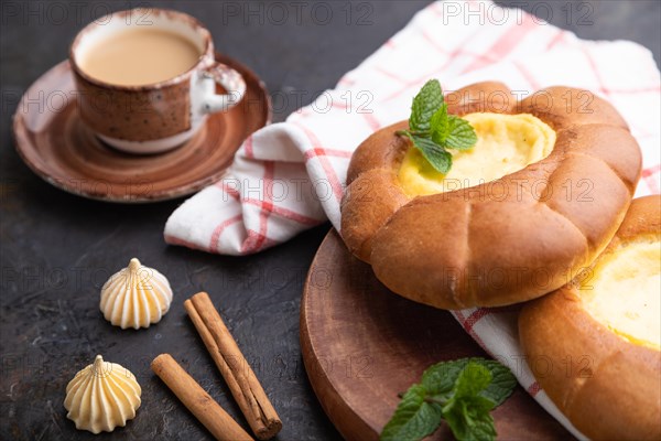 Sour cream bun with cup of coffee on a black concrete background and linen textile. Side view, close up, selective focus