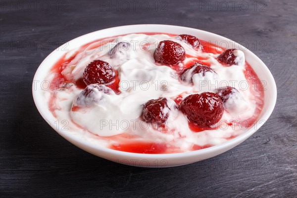 White plate with greek yogurt and strawberry jam on black wooden background. close up