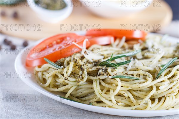 Spaghetti pasta with pesto sauce, tomatoes and cheese on a linen tablecloth. close up, selective focus