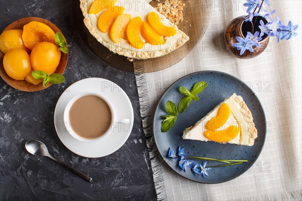 A piece of peach cheesecake on a blue ceramic plate with blue flowers and a cup of coffee on a linen napkin on a black concrete background. top view, close up