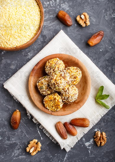 Energy ball cakes with dried apricots, sesame, cornflakes, linen, walnuts and dates with green mint leaves in a wooden bowl on a black concrete background. linen napkin, top view, close up, flat lay. vegan homemade candy