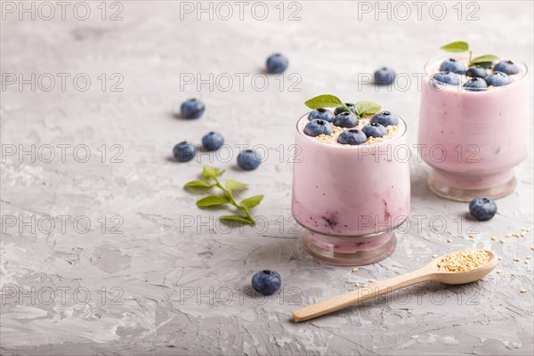 Yoghurt with blueberry and sesame in a glass and wooden spoon on gray concrete background. side view, copy space, selective focus