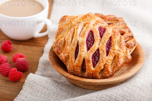 Puff pastry buns with strawberry jam on wooden background with linen textile and a cup of coffee. side view, close up, selective focus
