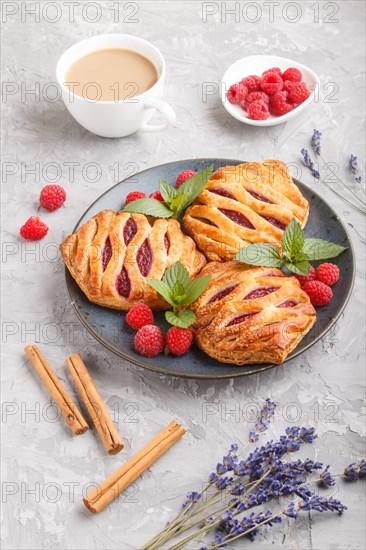 Puff pastry buns with strawberry jam on blue ceramic plate on gray concrete background, cup of coffee, lavender, cinnamon, mint leaves. side view, close up