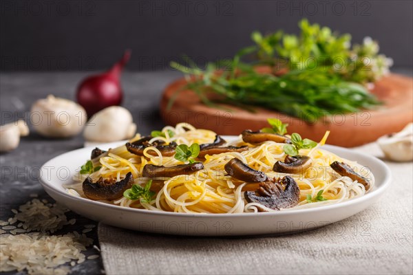 Rice noodles with champignons mushrooms, egg sauce and oregano on white ceramic plate on a black concrete background. side view, selective focus, close up