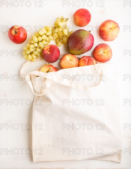 Fruits in reusable cotton textile white bag. Zero waste shopping, storage and recycling concept, eco friendly lifestyle. Top view, flat lay, copy space. Peach, apple, mango, grape